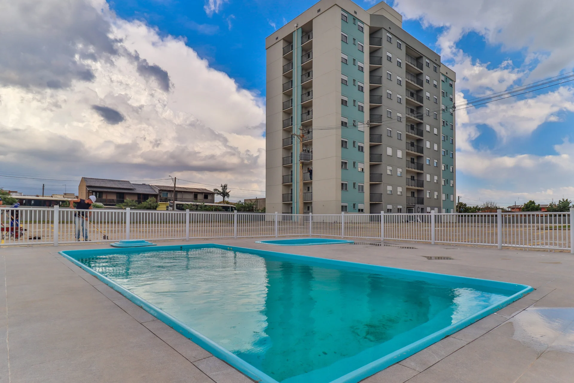 Foto das piscinas adulto e infantil cheias do Residencial Capri, com a torre ao fundo