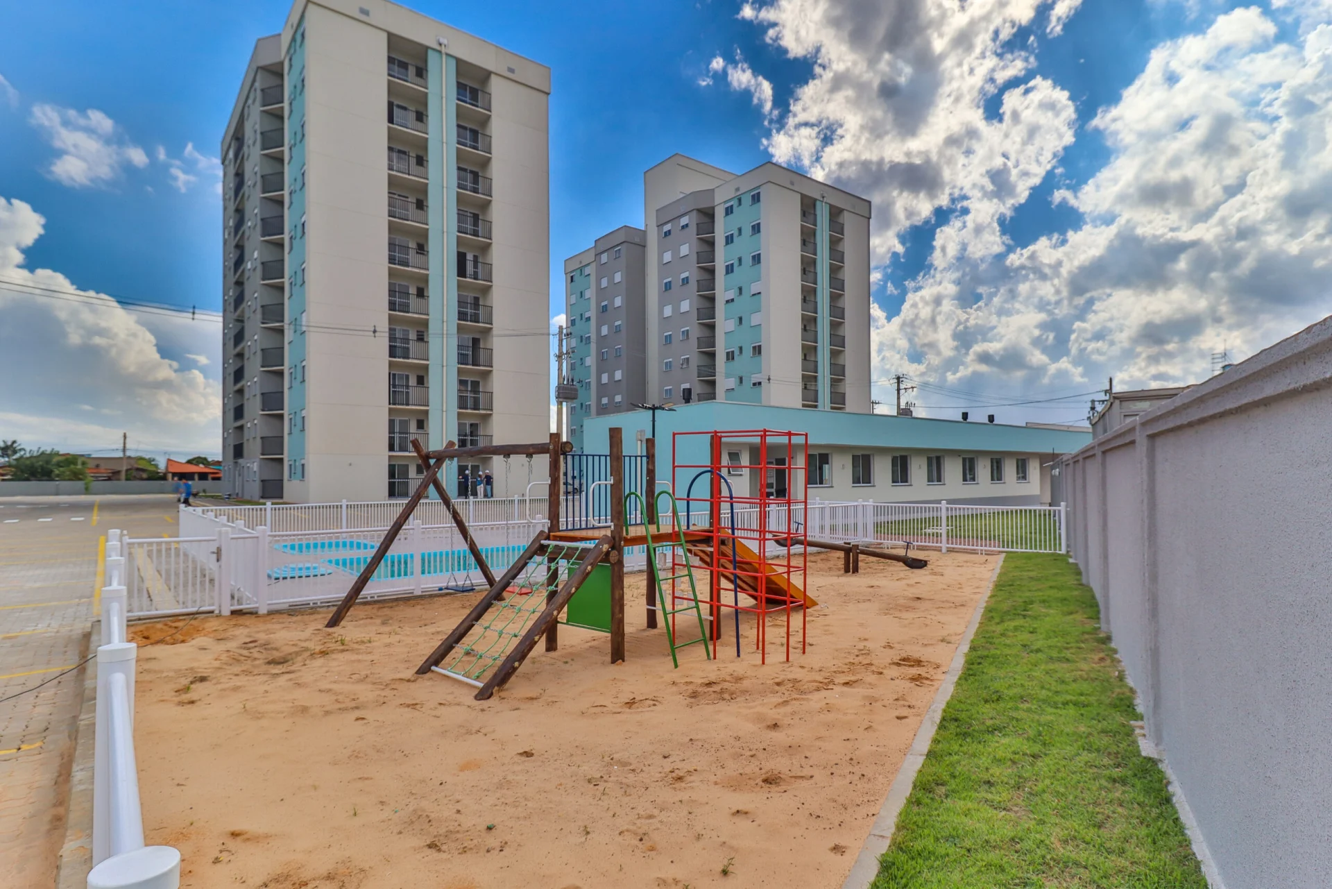 Foto do playground do Residencial Capri com a piscina e as torres ao fundo